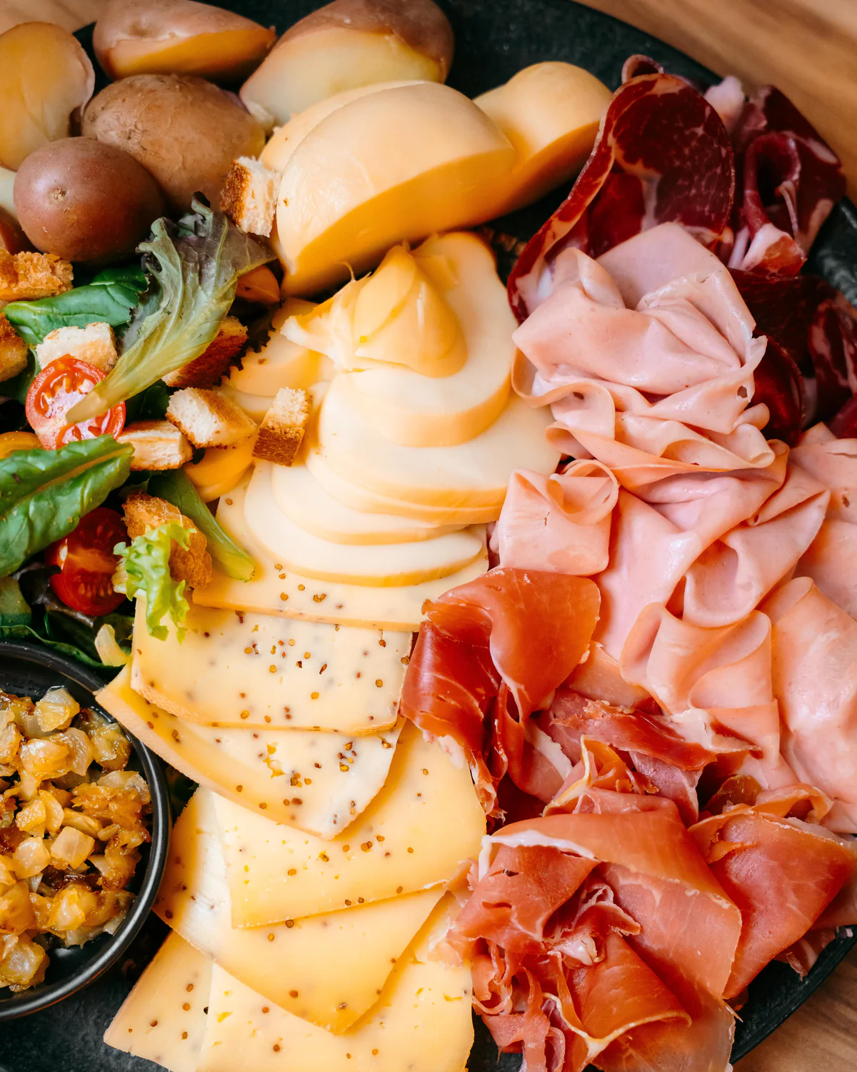 Planche garnie de charcuteries, de fromages en tranches, de salade, de croûtons et de pommes de terre, vue de dessus