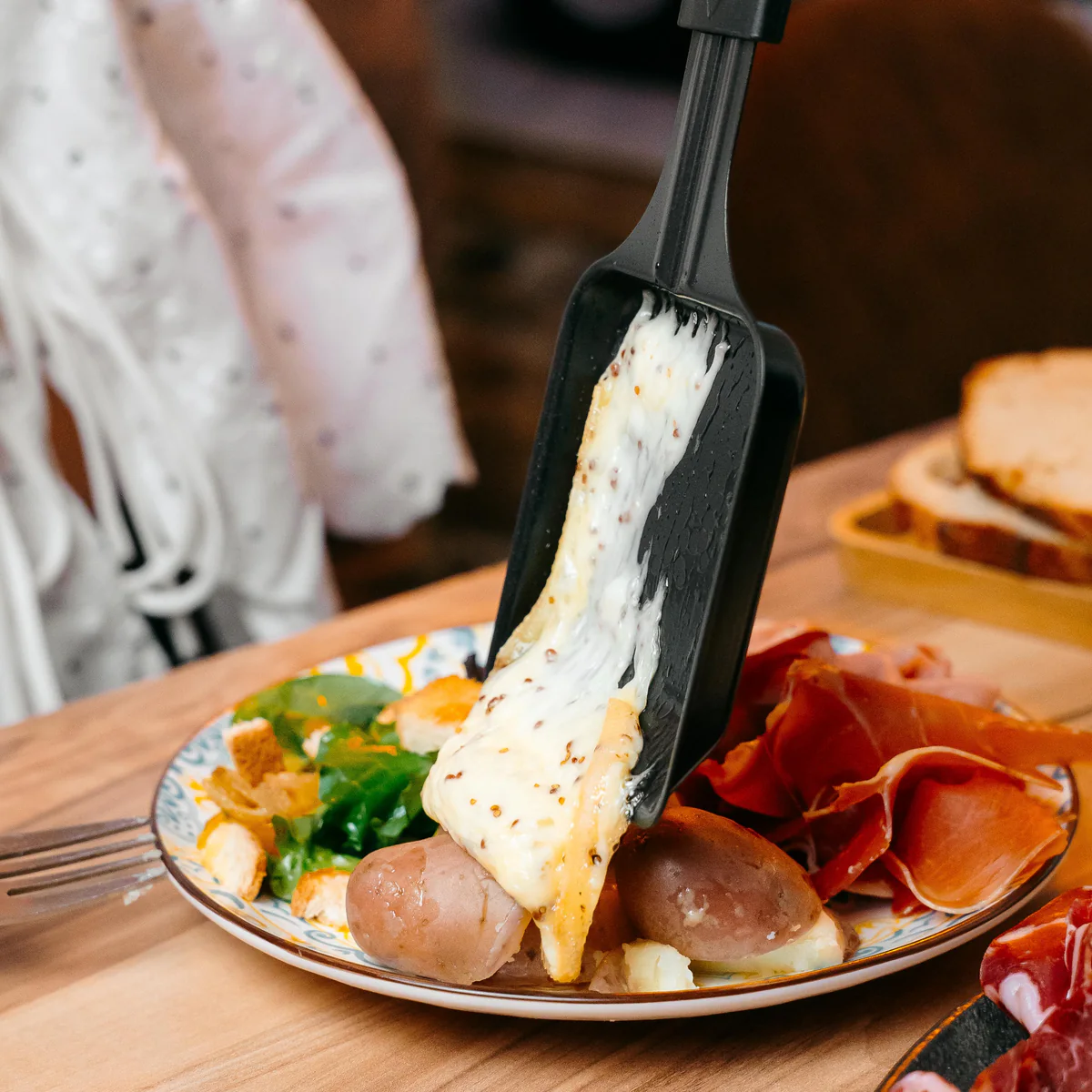 Poêlon de fromage fondu versé sur les pommes de terre d'une assiette garnie