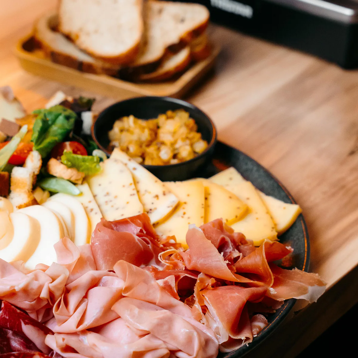 Planche de charcuteries et de fromages, pain grillé et appareil à raclette sur une table en bois